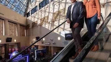 A man and a woman on an escalator in a modern building with a glass ceiling and multiple windows.