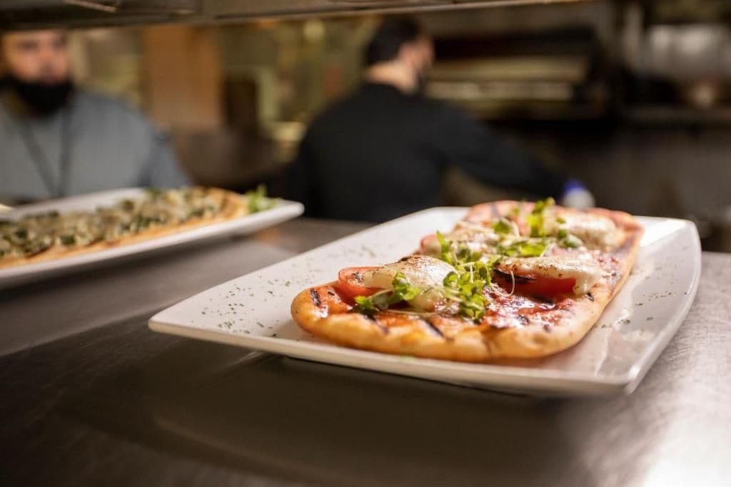 A pizza on a white plate with toppings, in a restaurant setting.