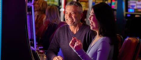 Una pareja jugando una máquina tragamonedas en un casino con mucha iluminación.