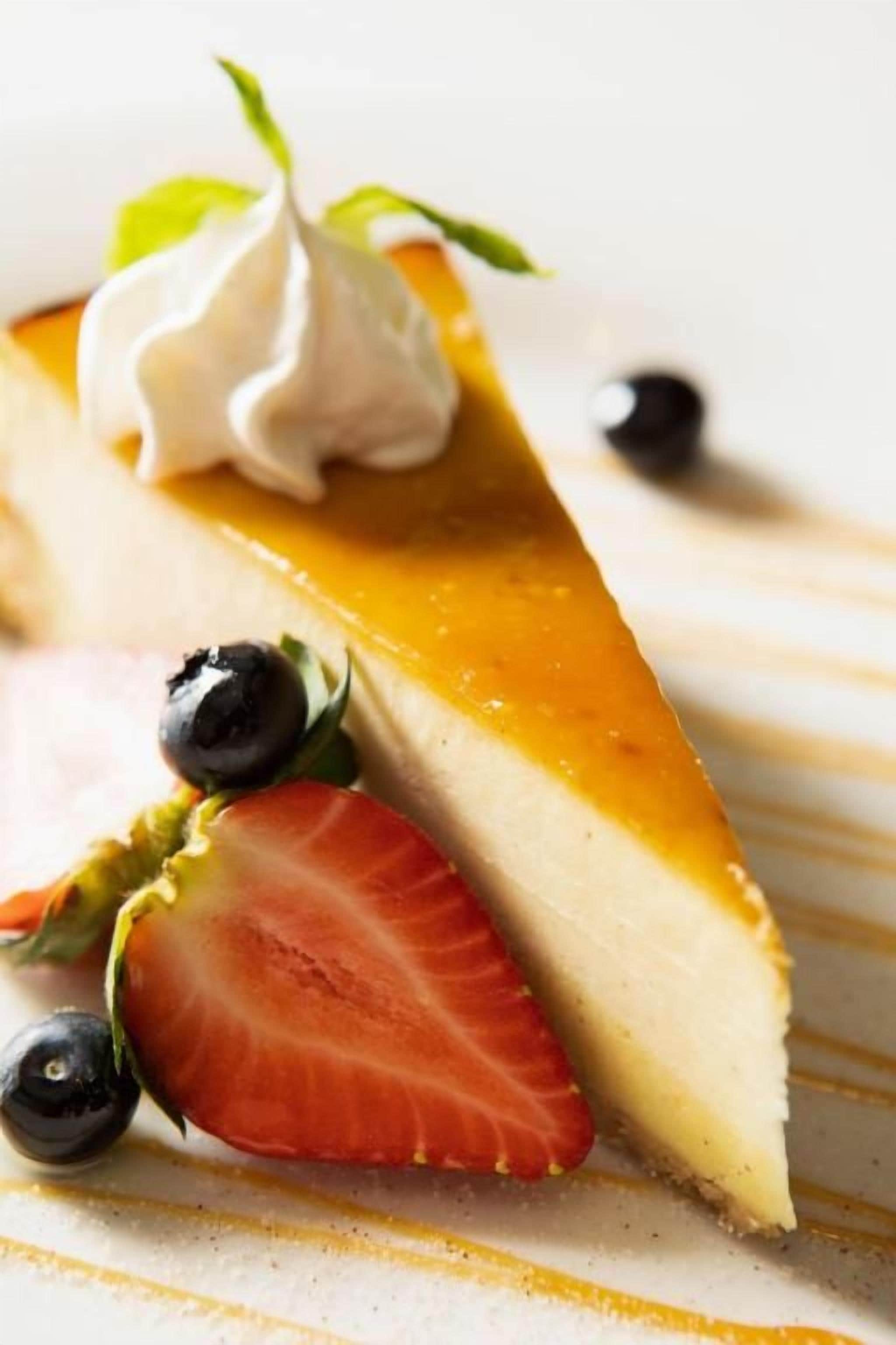 A slice of cheesecake with a caramel topping and a dollop of whipped cream, accompanied by a strawberry and blueberries.