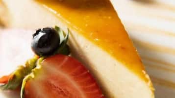 A slice of cheesecake with a caramel topping and a dollop of whipped cream, accompanied by a strawberry and blueberries.