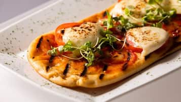 A rectangular plate with a grilled pizza topped with tomatoes, cheese, and greens.