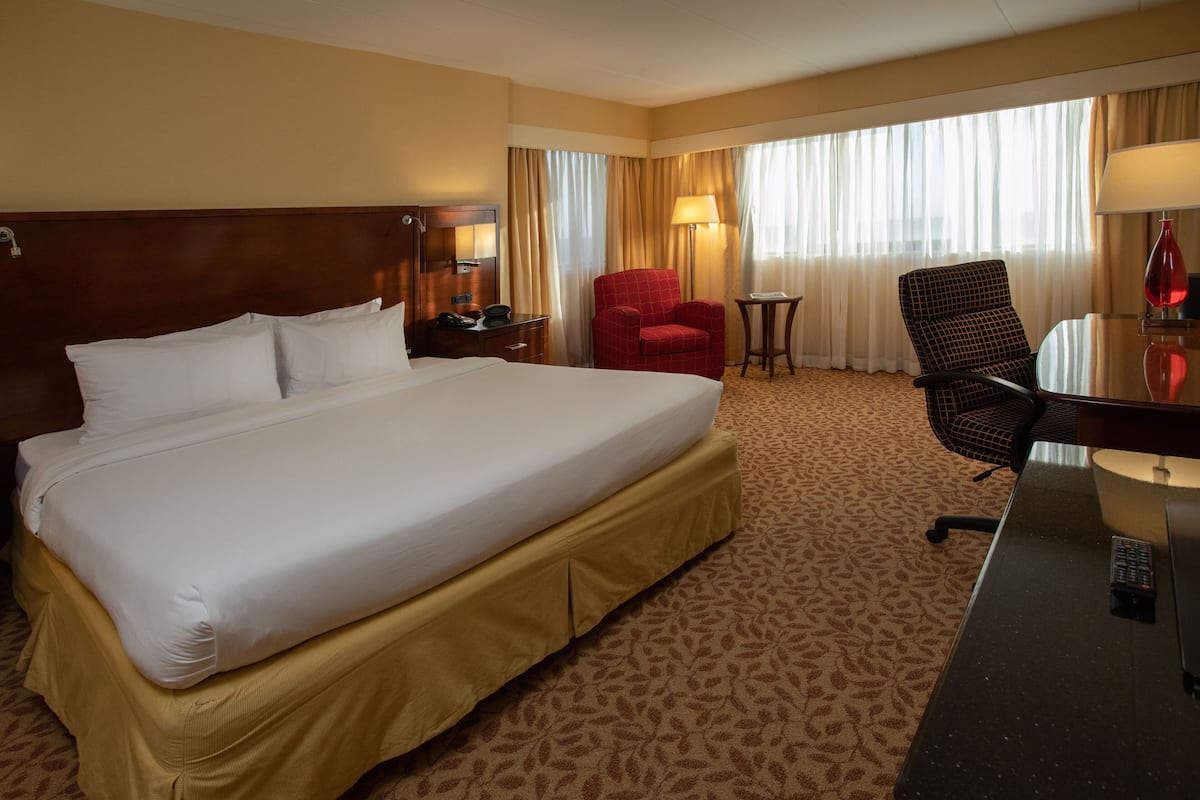 Una habitación de hotel con una cama grande, un escritorio, un sillón rojo y una pequeña mesa.