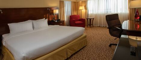 A hotel room with a large bed, a desk, a red armchair, and a small table.