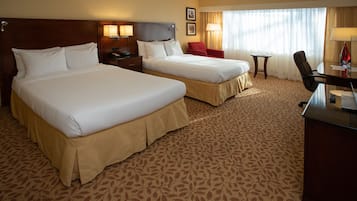 A hotel room with two beds, a desk, a chair, and a small table.