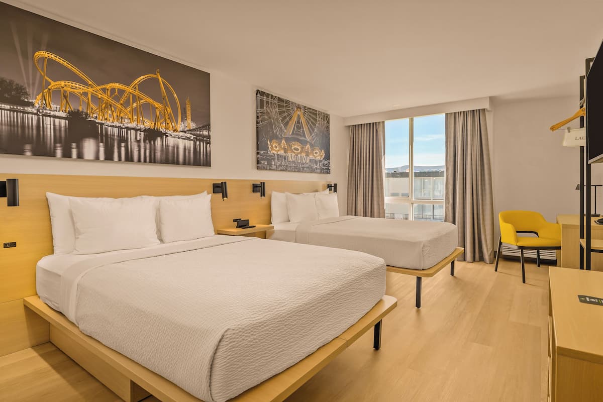 A hotel room with two beds, a desk, a chair, and artwork on the walls.