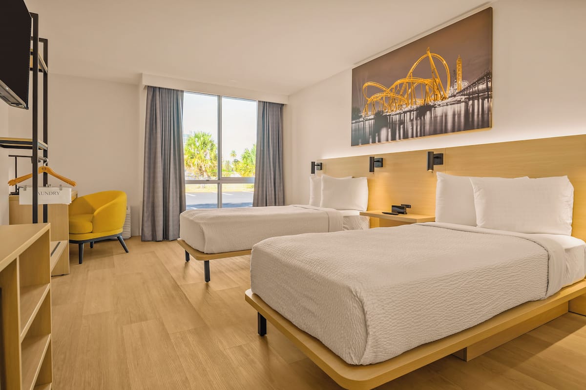 A hotel room with two beds, a desk, a chair, and a large window with a view of palm trees.