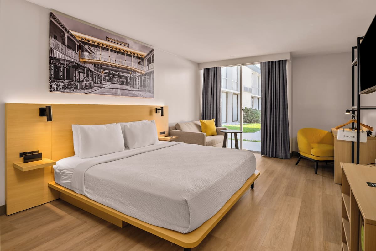 A modern hotel room with a large bed, a desk, a chair, and a window with curtains.