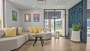 A modern lobby with a grey sofa, yellow cushions, a round table, and a large potted plant. - B&B Hotel Orlando International Drive Near Universal - Newly Renovated! (Orlando)