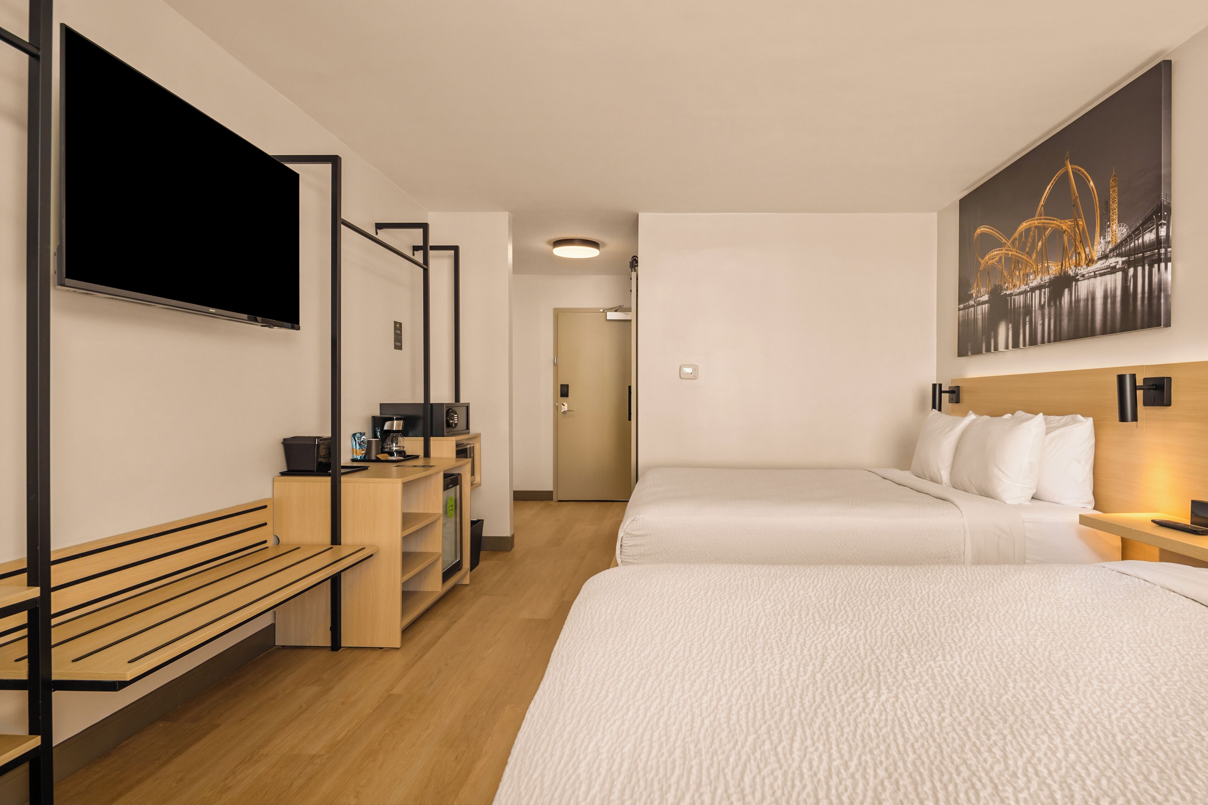 Habitación de hotel con cama, escritorio, computadora, televisor y banca.