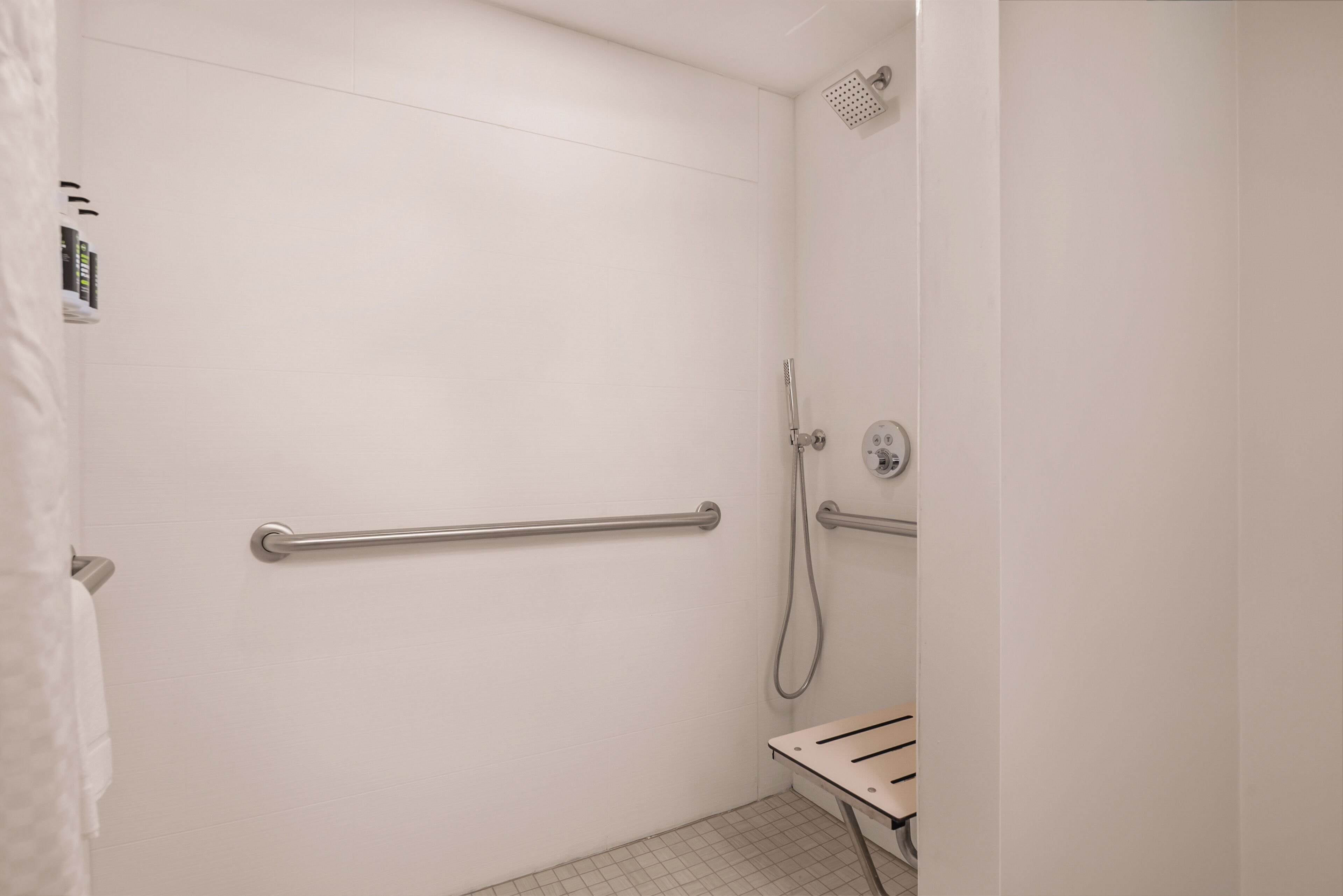 A white bathroom with a shower, grab bars, and a towel rack.