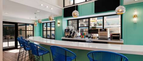 Un área de bar moderna con taburetes azules, una barra blanca y una cocina al fondo.