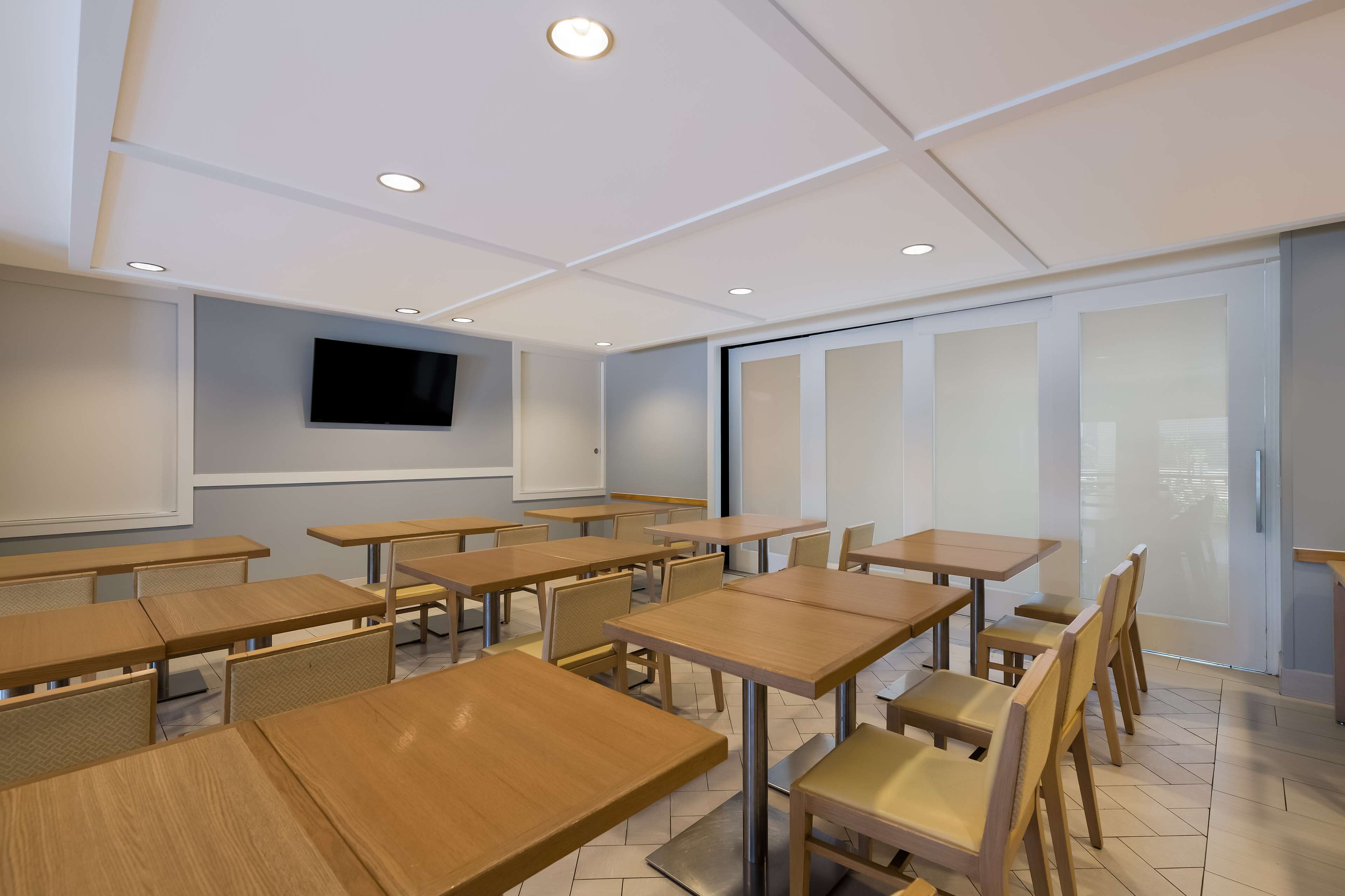 A classroom with wooden desks and chairs, a whiteboard, and a TV mounted on the wall.