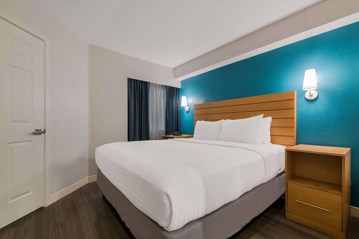 Quarto de hotel com cama grande, cabeceira de madeira, duas mesas de cabeceira e um criado-mudo.