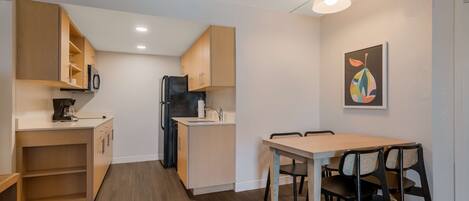 A compact kitchen with wooden cabinets, a refrigerator, a microwave, and a dining area with a table and chairs.