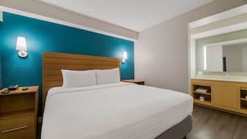 A hotel room with a large bed, wooden headboard, two bedside tables with lamps, a bathroom with a mirror and sink, and a teal accent wall.