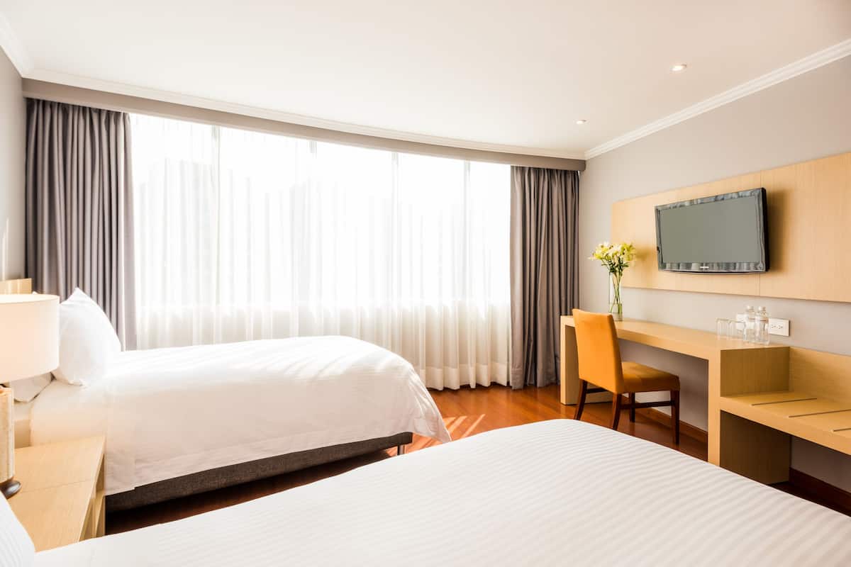 Een hotelkamer met twee bedden, een bureau, een stoel, een televisie en een raam met gordijnen.