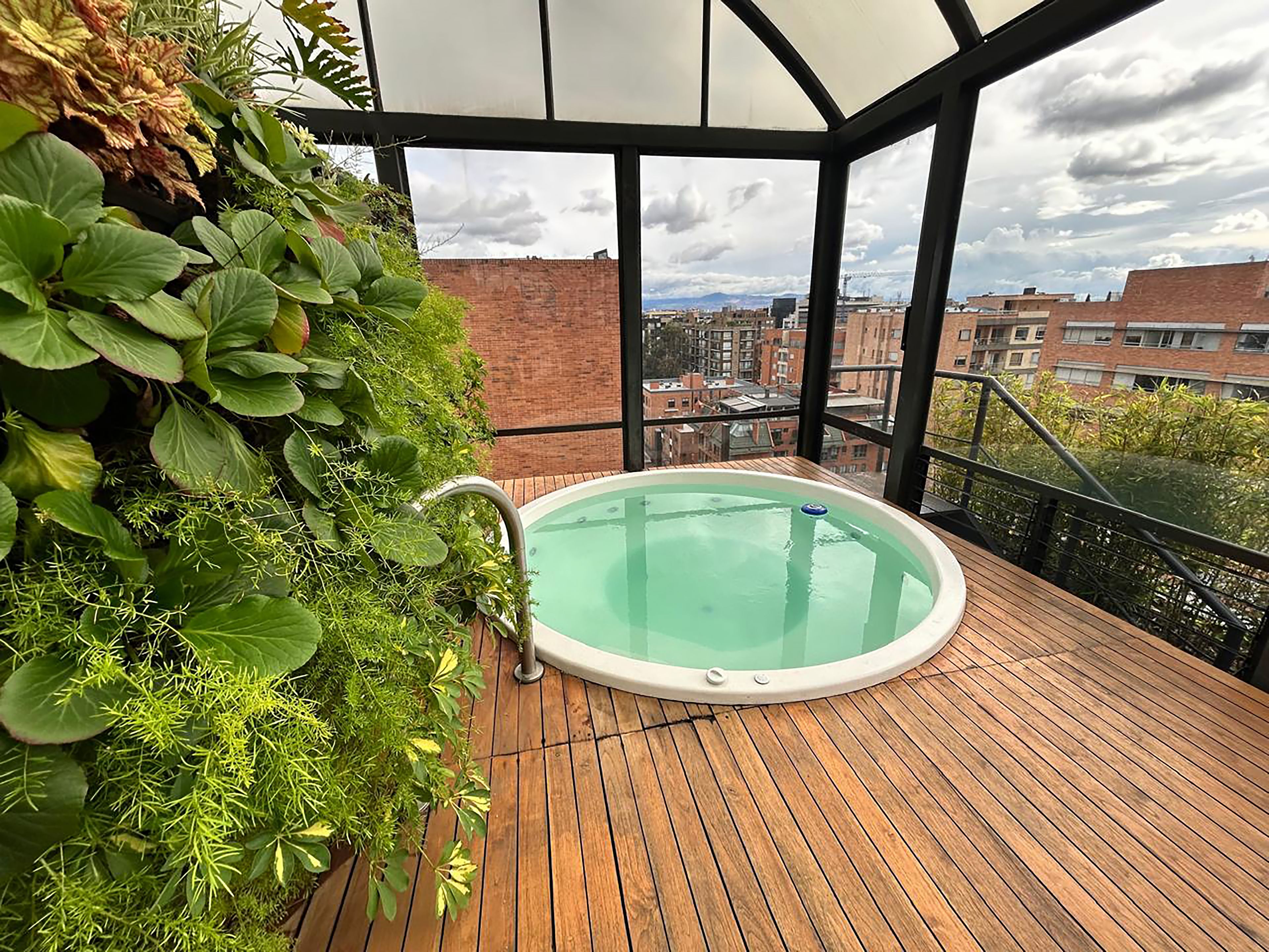 A hot tub on a wooden deck with a view of buildings and a cloudy sky.