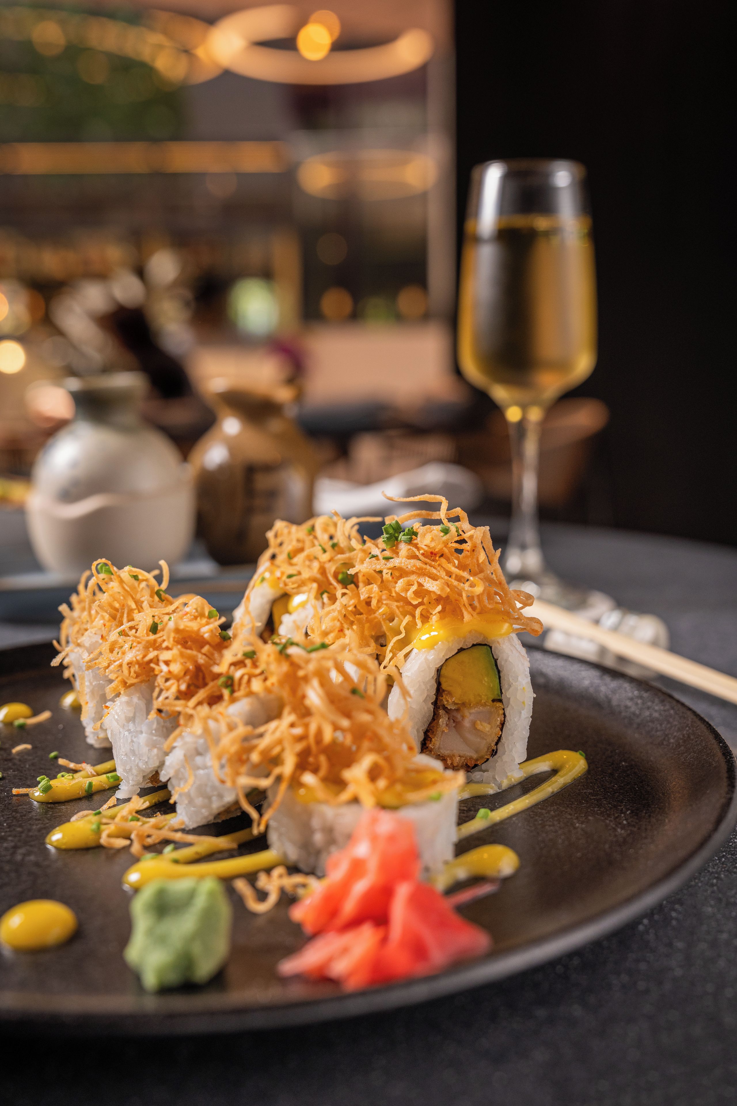 A plate of sushi with toppings and a glass of white wine on a dark table.