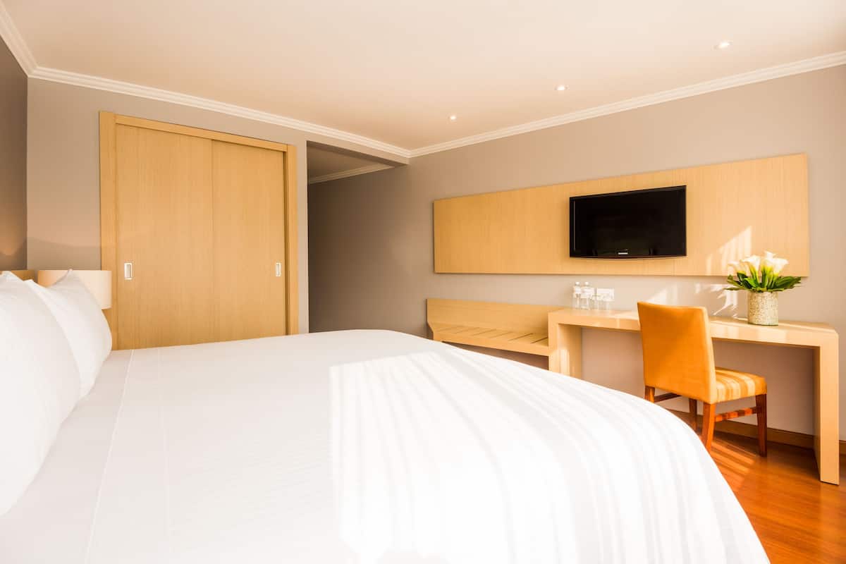 Een hotelkamer met een groot bed, een bureau met stoel, een aan de muur bevestigde televisie en een houten garderobe.