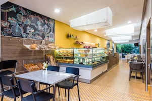 Una cafetería con un muro de pizarra, una vitrina con pasteles y un suelo a cuadros.