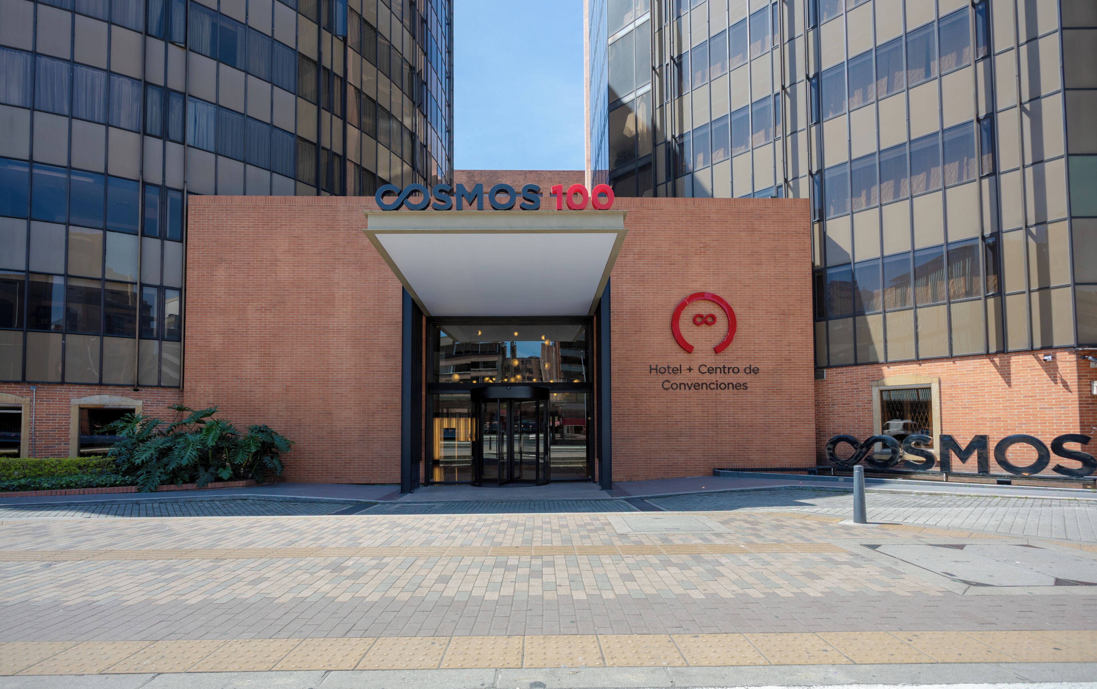 A hotel entrance with a modern glass facade, a prominent 'COSMOS 100' sign, and a wheelchair-accessible entrance.