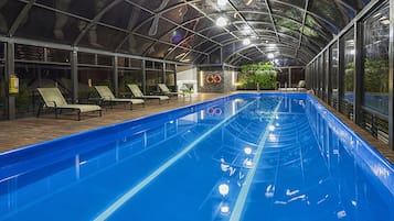 Una piscina interior con techo de vidrio, sillas de descanso y una pequeña cascada.