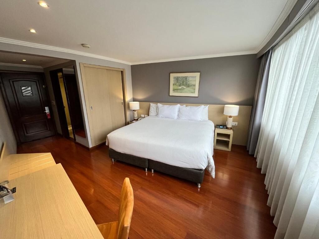 Una camera d'albergo con un letto grande, lampade sui comodini, una scrivania in legno e una sedia.