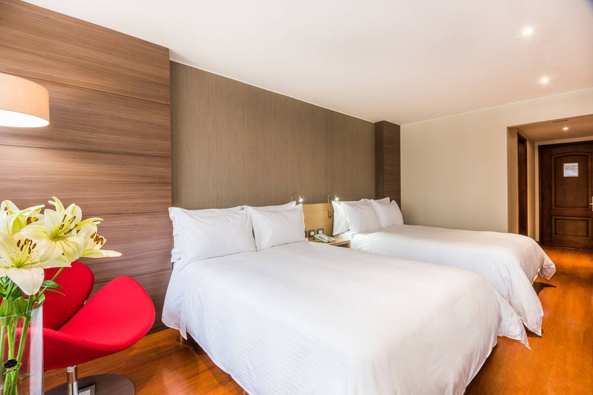 Een hotelkamer met twee bedden, een rode stoel en een bloemenvaas.