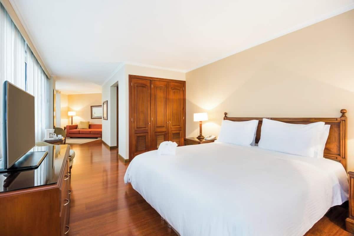 Een hotelkamer met een groot bed, een houten garderobe, een televisie en een bank op de achtergrond.