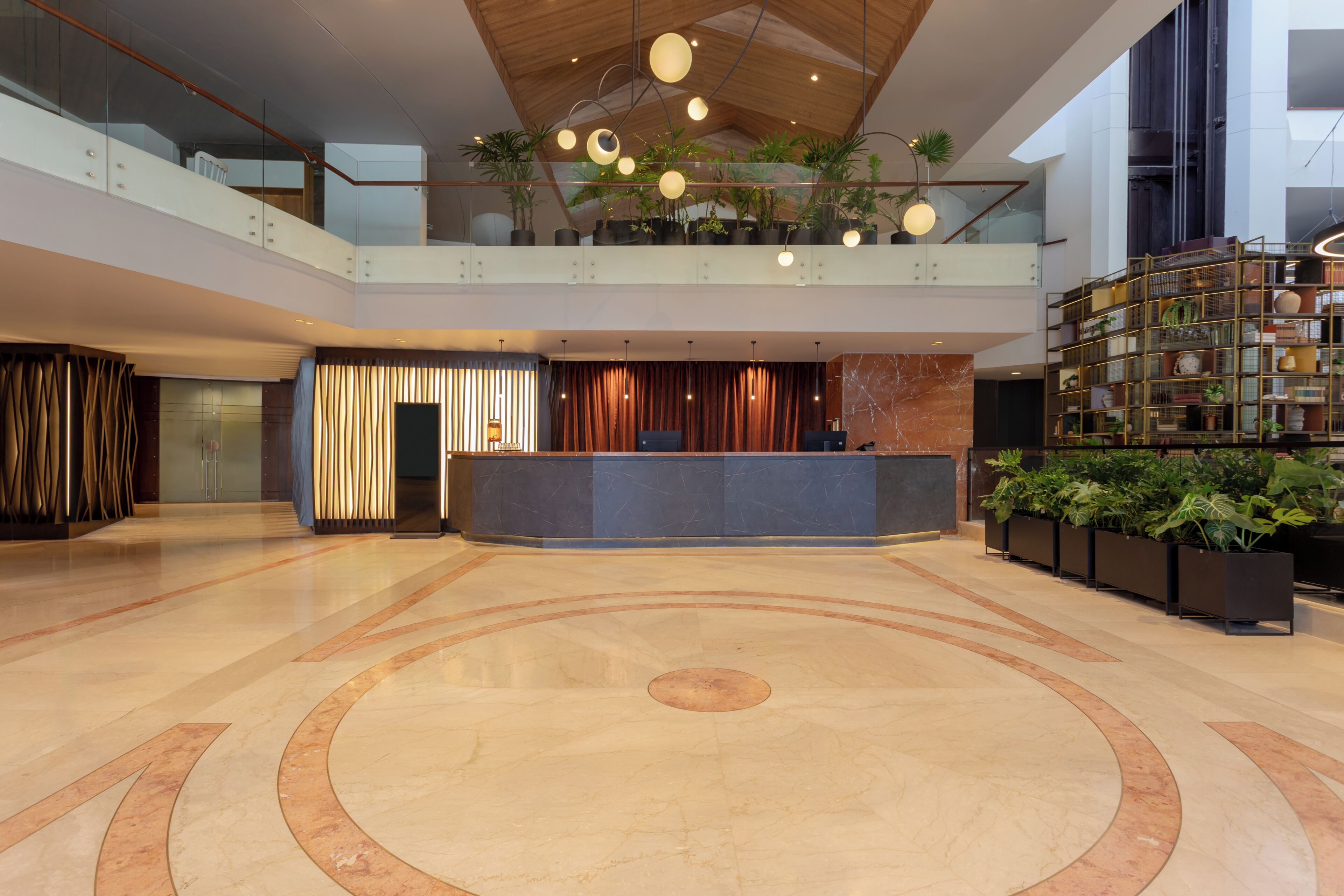 Un vestíbulo amplio con un mostrador de recepción central, un techo alto con iluminación moderna y una extensa área de plantas de interior.