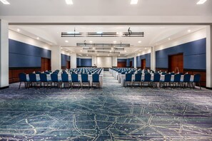 Une salle de conférence avec des rangées de tables et de chaises, une moquette à motifs et un design de plafond moderne.