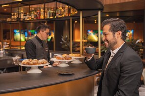 A bar area with a counter, a person holding a cup, and pastries on display.