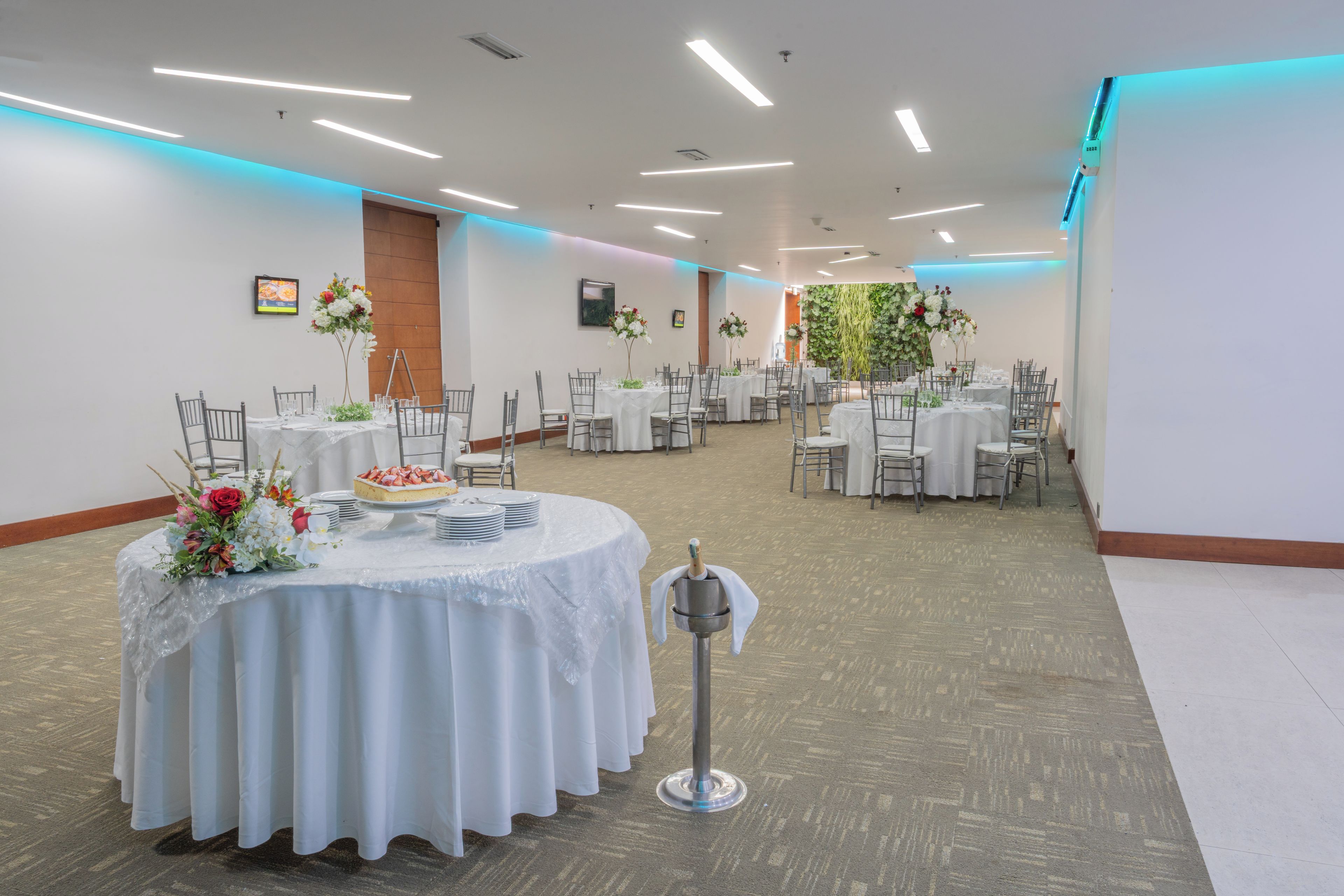 A banquet hall with round tables, chairs, and a central floral arrangement.