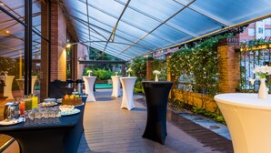 Une terrasse extérieure dotée d’un toit en verre, de tables recouvertes de nappes blanches et de plantes en pot.