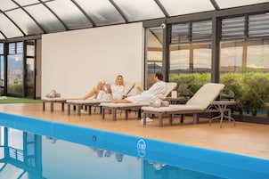 Zona junto a la piscina con sillas de descanso y un recinto de cristal.