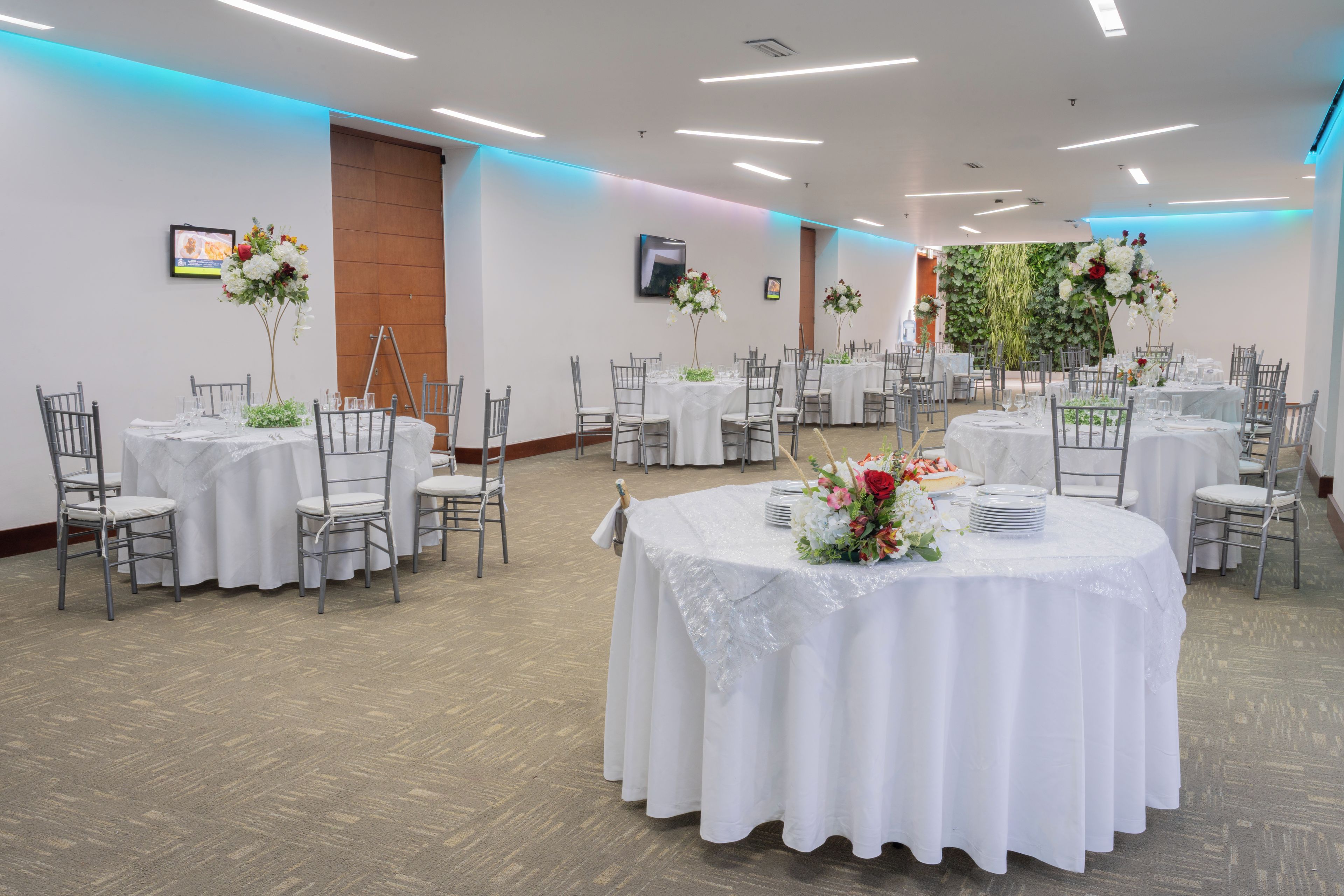 Ein Festsaal mit runden Tischen, Stühlen und Blumenarrangements.