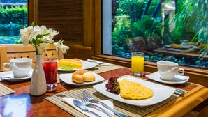 Une table de petit-déjeuner avec des assiettes remplies de nourriture, une carafe de jus et un vase de fleurs.