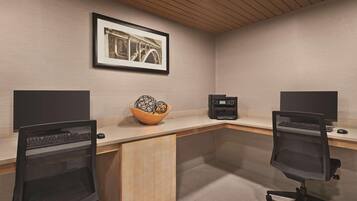 Un ufficio moderno con due postazioni da lavoro, ciascuna dotata di monitor, tastiera e mouse. Al centro, una scrivania in legno con una ciotola decorativa sopra. La stanza presenta un soffitto in legno e un quadro appeso al muro.
