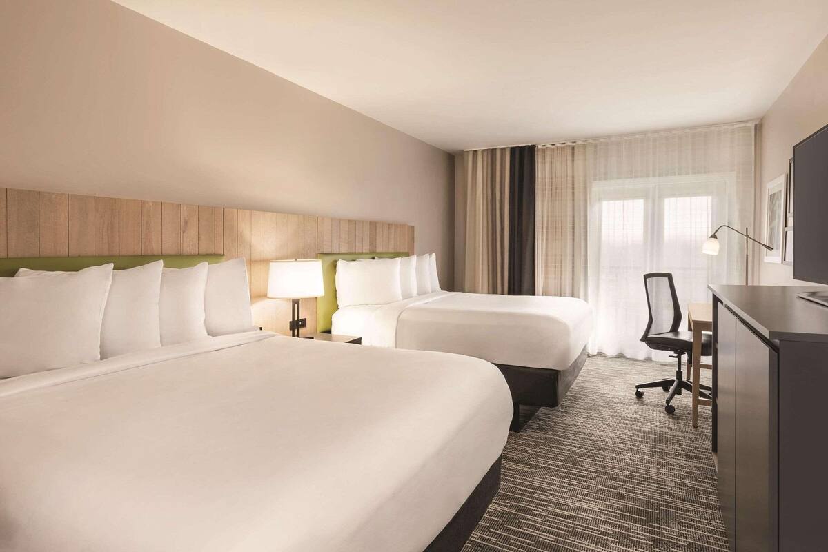 A hotel room with two beds, a desk, a chair, and a television.