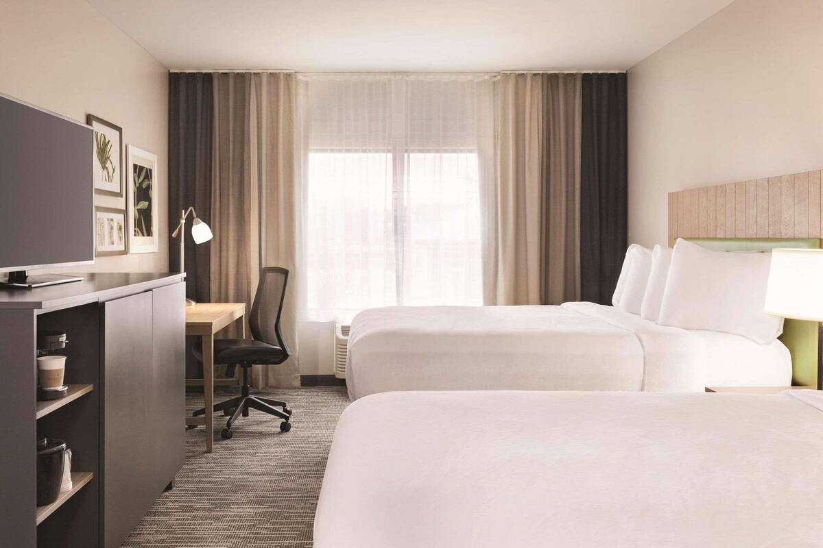 A hotel room with two beds, a desk, a chair, and a television.