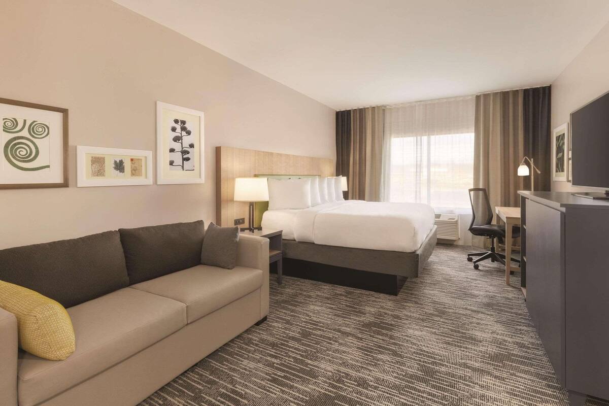 A hotel room with a bed, a sofa, a desk, and a television.