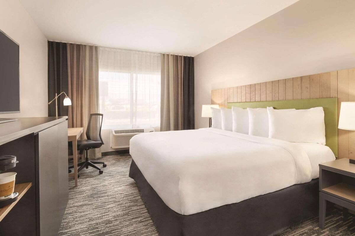 A hotel room with a large bed, a desk with a chair, a TV, and a window with curtains.