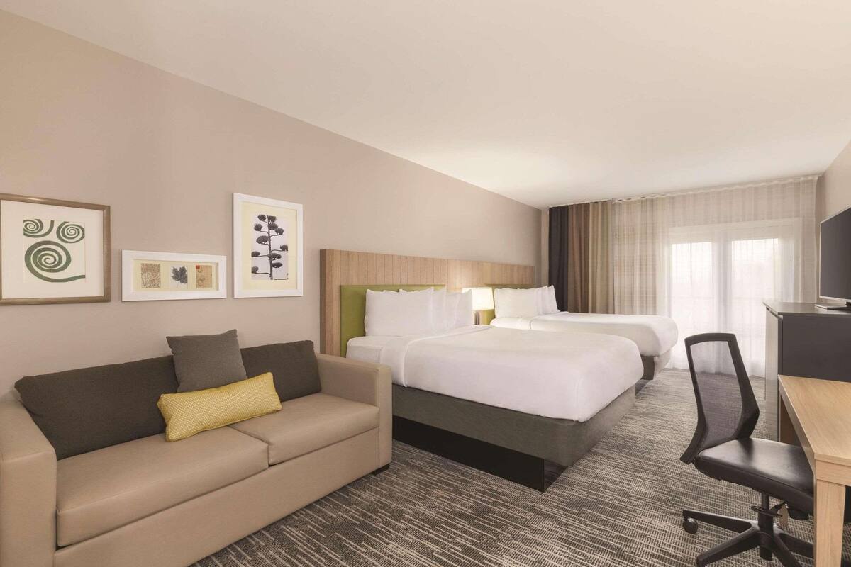 A hotel room with a bed, a sofa, a desk, and artwork on the walls.