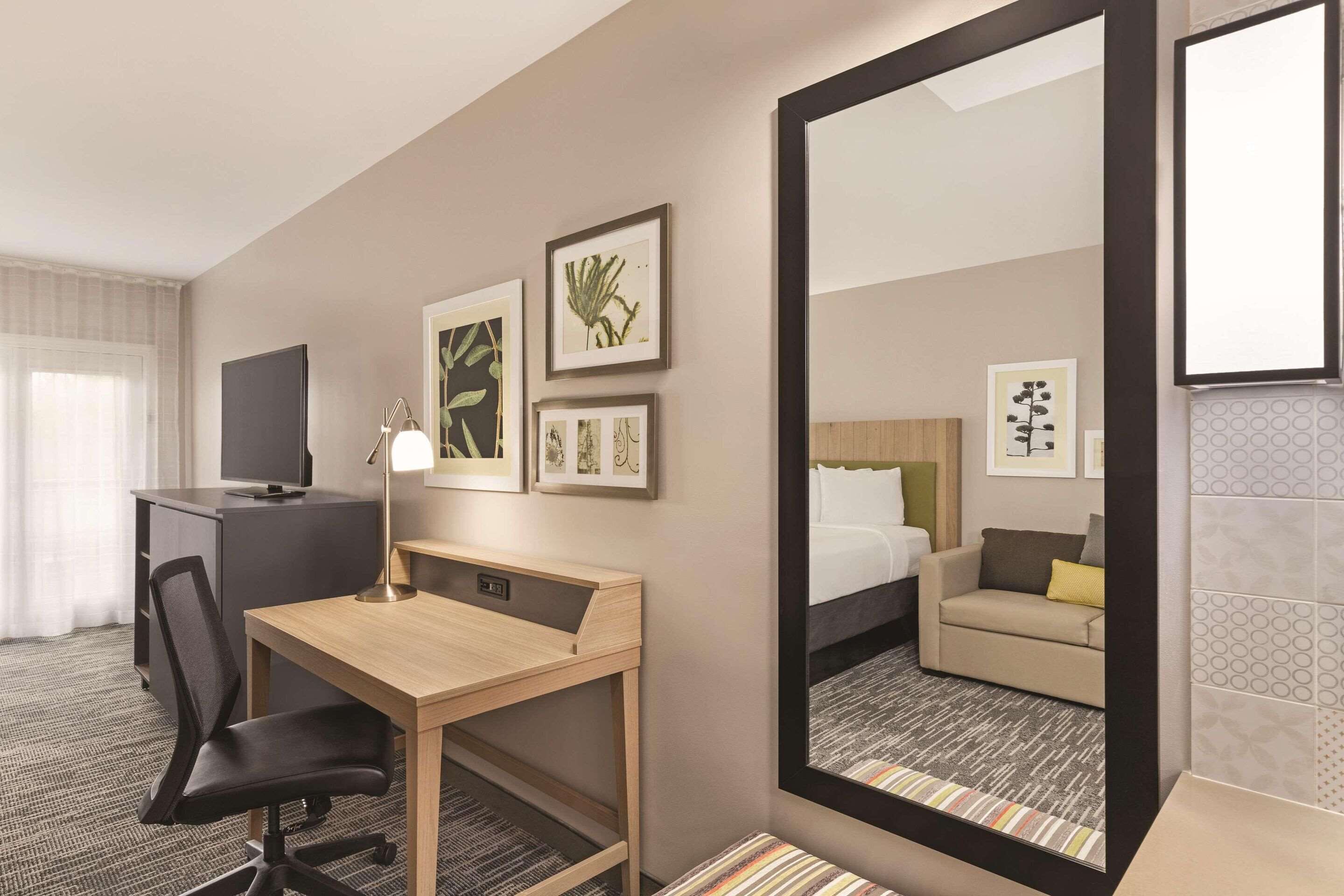 Ein Hotelzimmer mit Schreibtisch, Stuhl, Fernseher und einem Kunstwerk an der Wand.