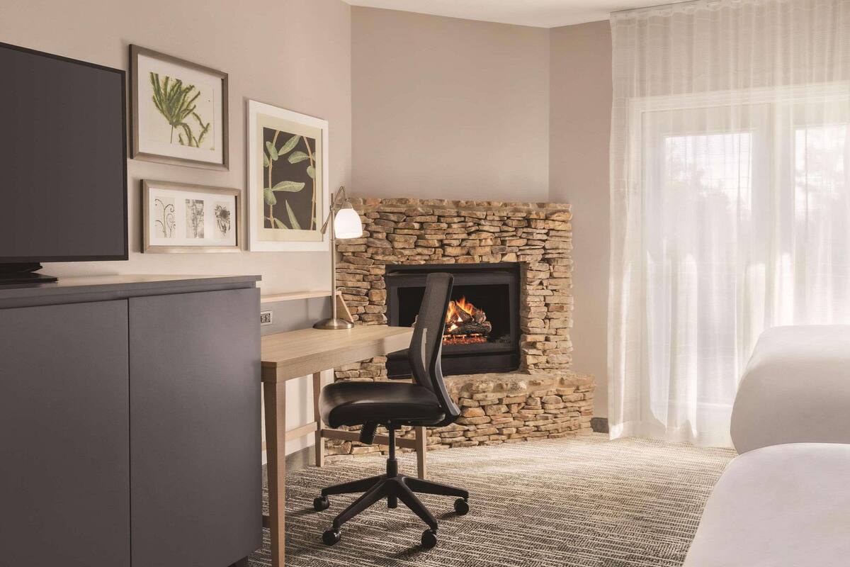 A hotel room with a stone fireplace, a desk with a chair, and artwork on the wall.