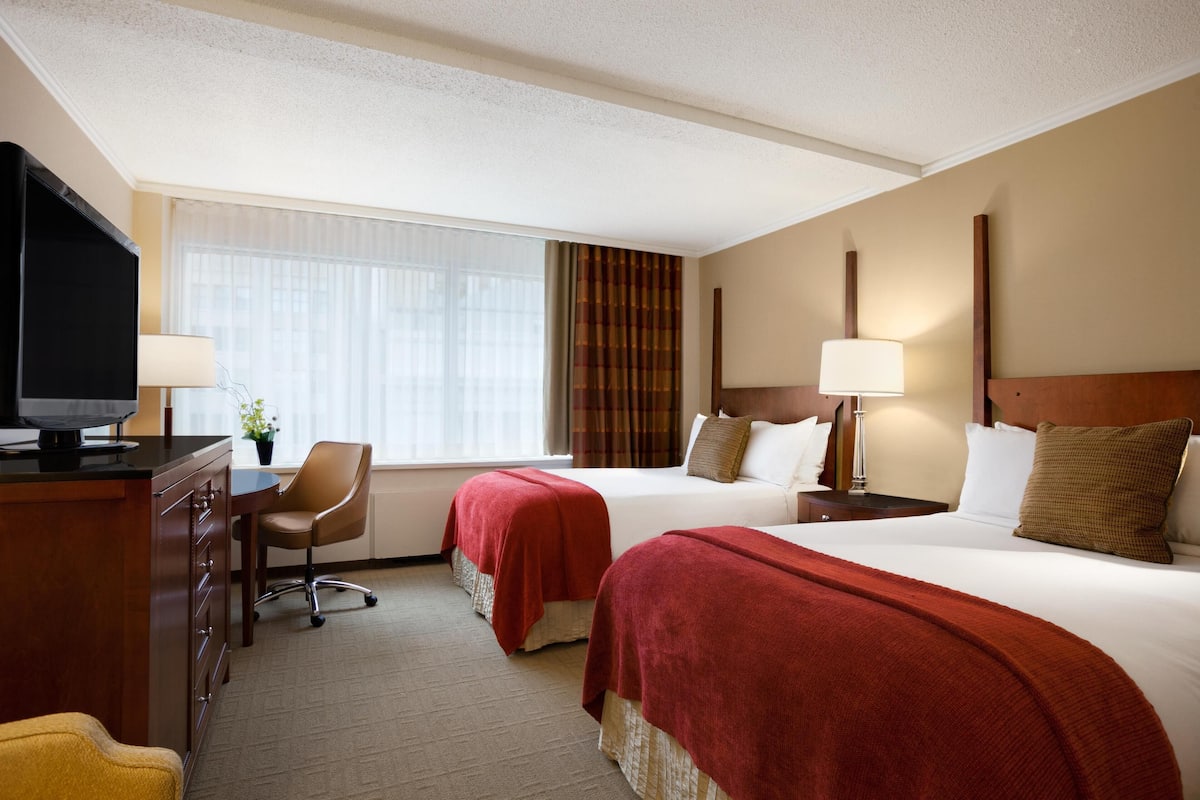 A hotel room with two beds, a desk with a TV, a chair, and a window with curtains.