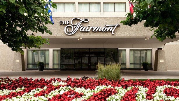 A hotel entrance with a sign reading "The Fairmont" and a flower bed in front.