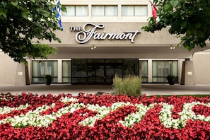 A hotel entrance with a sign reading "The Fairmont" and a flower bed in front.