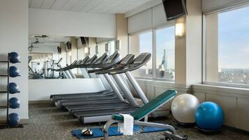 Un gimnasio con cintas de correr, balones de ejercicio y vistas a un paisaje urbano a través de amplias ventanas.